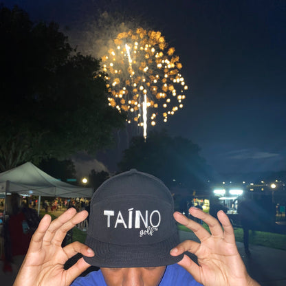 Black Taino Golf with white embroidered logo, displayed in front of a July 4th fireworks show.