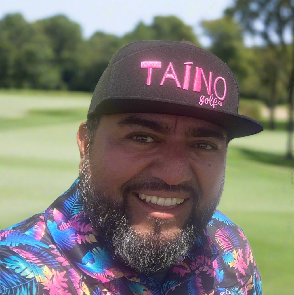 Golfer wearing black Taino Golf hat with pink logo on a golf course.